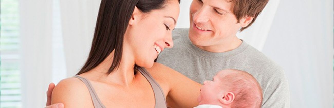 Mutter hält Baby im Arm, Vater schaut Mutter an